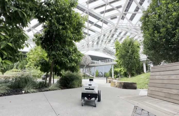 A black and white mobile robot using ReMEmbR rolling along a sidewalk with trees on both sides at NVIDIA headquarters. 