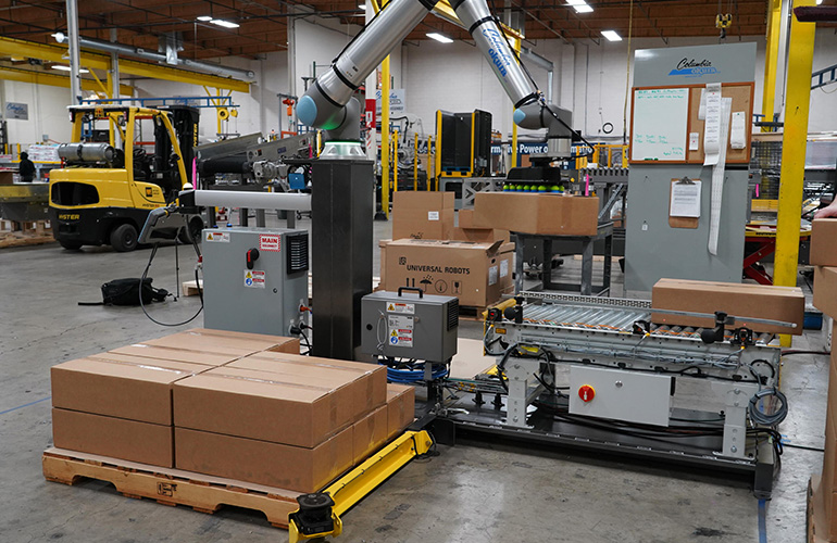 A Columbia/Okura miniPAL cobot system stacking boxes from a conveyor belt onto a pallet.