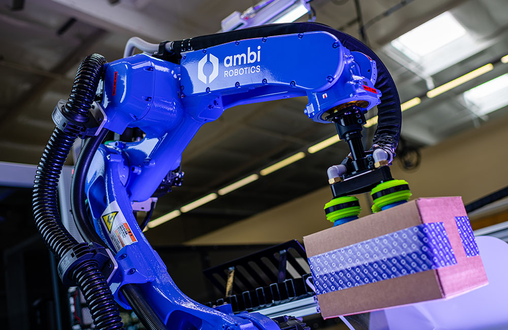 Ambi Robotics' AmbiSort A series picking a cardboard box with purple lighting. 